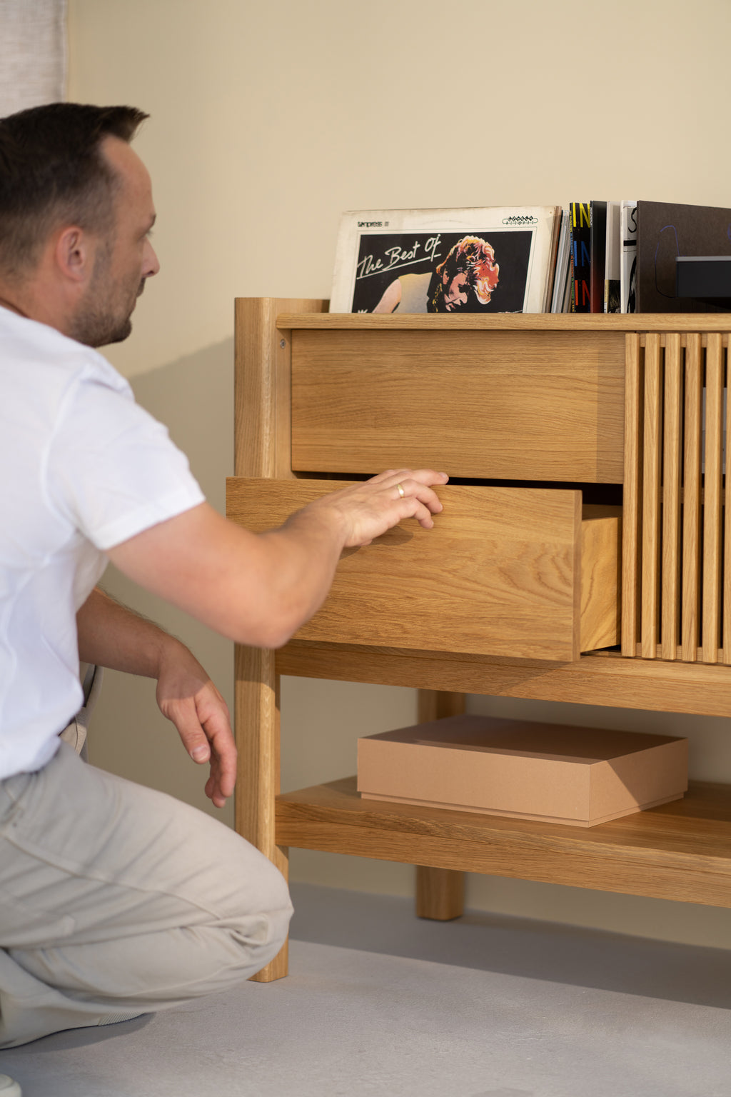 Man opening wooden cabinet drawer with vinyl records on top.