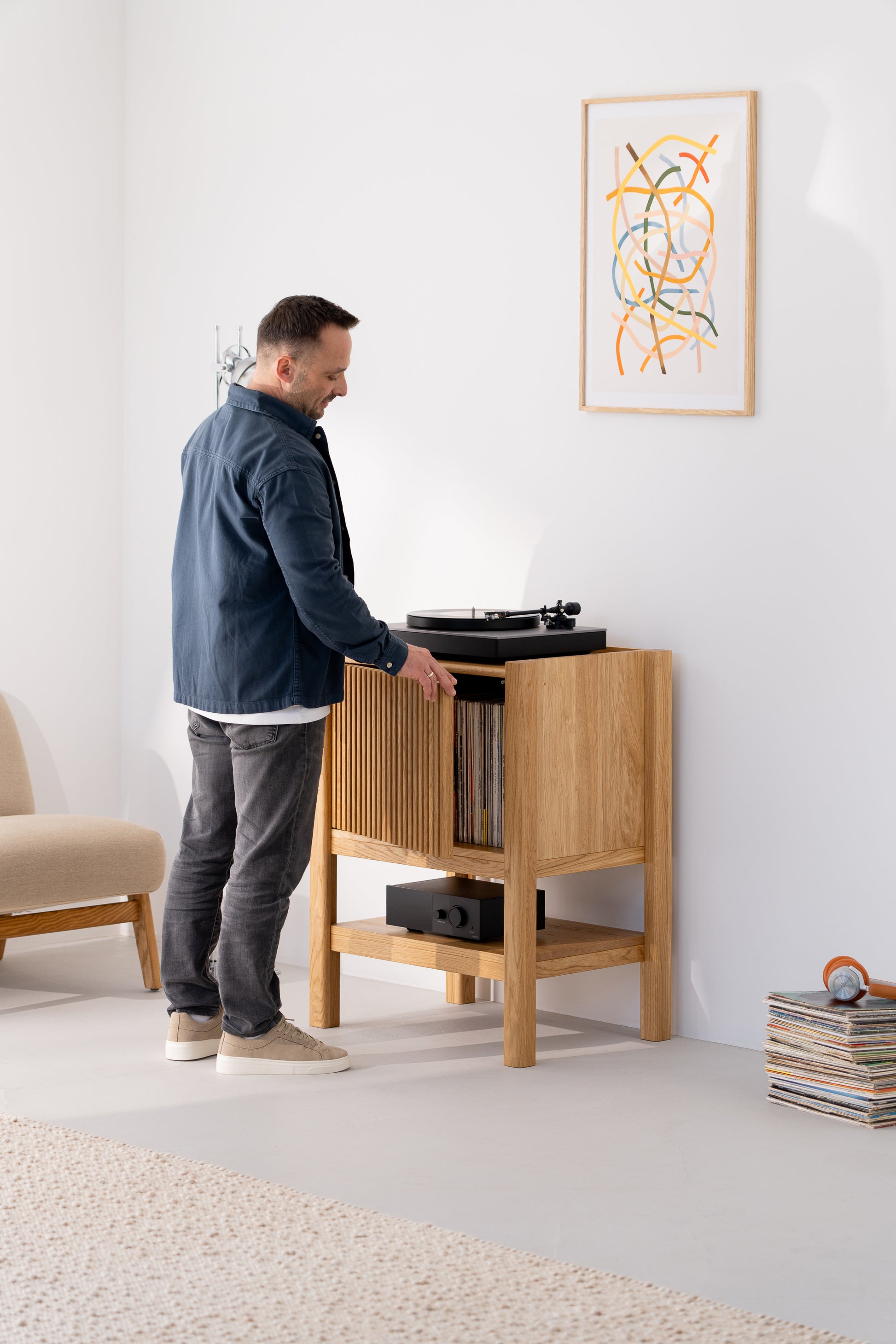 Man selecting a record from a wooden cabinet with a turntable on top in a minimalist room.