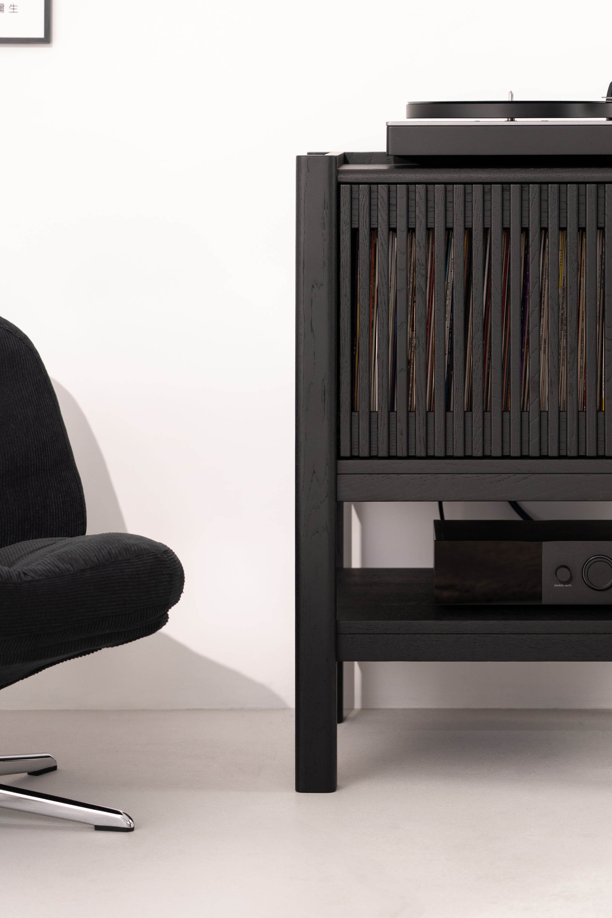 Black chair beside a dark wooden record cabinet with a turntable on top.
