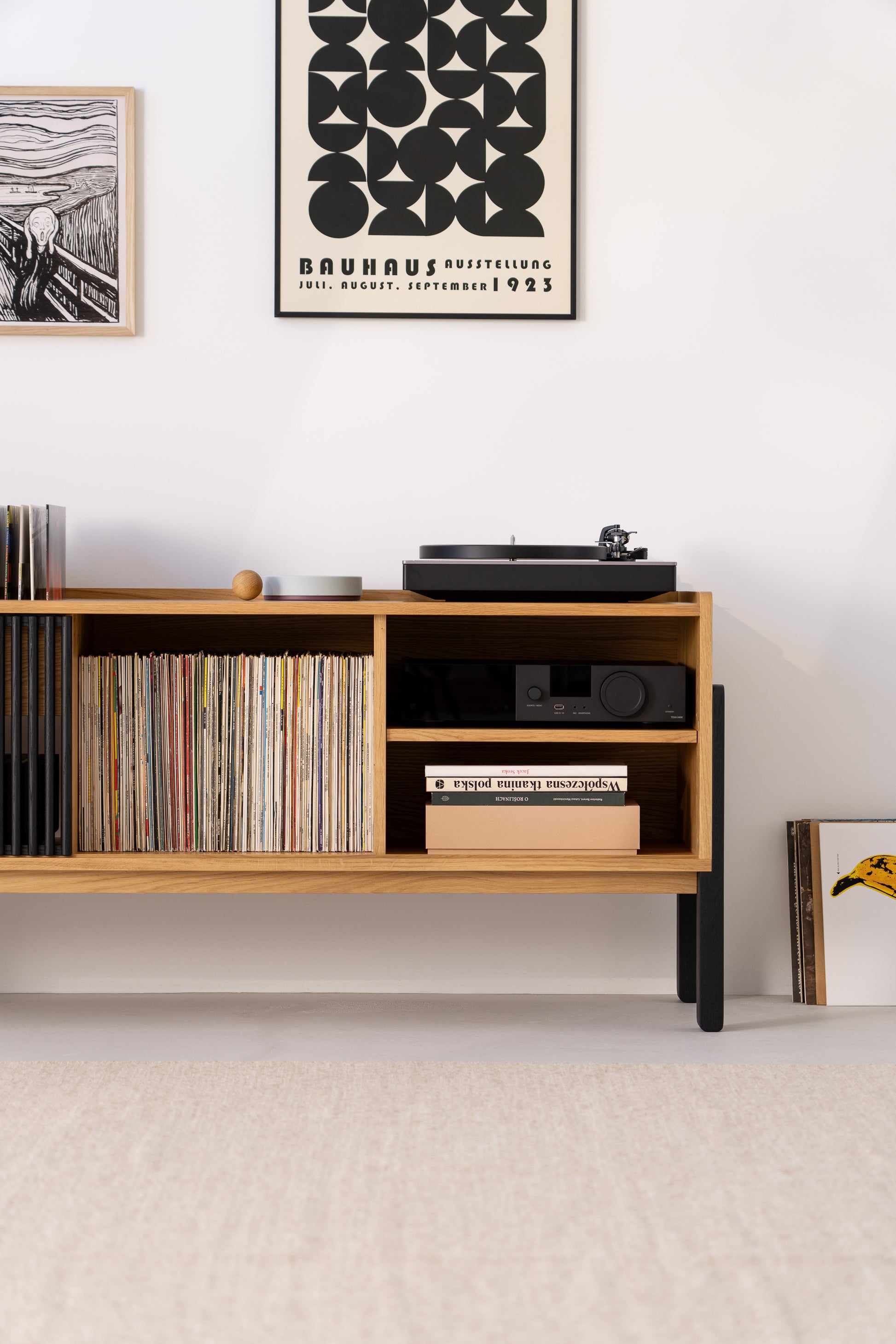Wooden shelf with vinyl records, books, a turntable, and framed prints on a white wall.