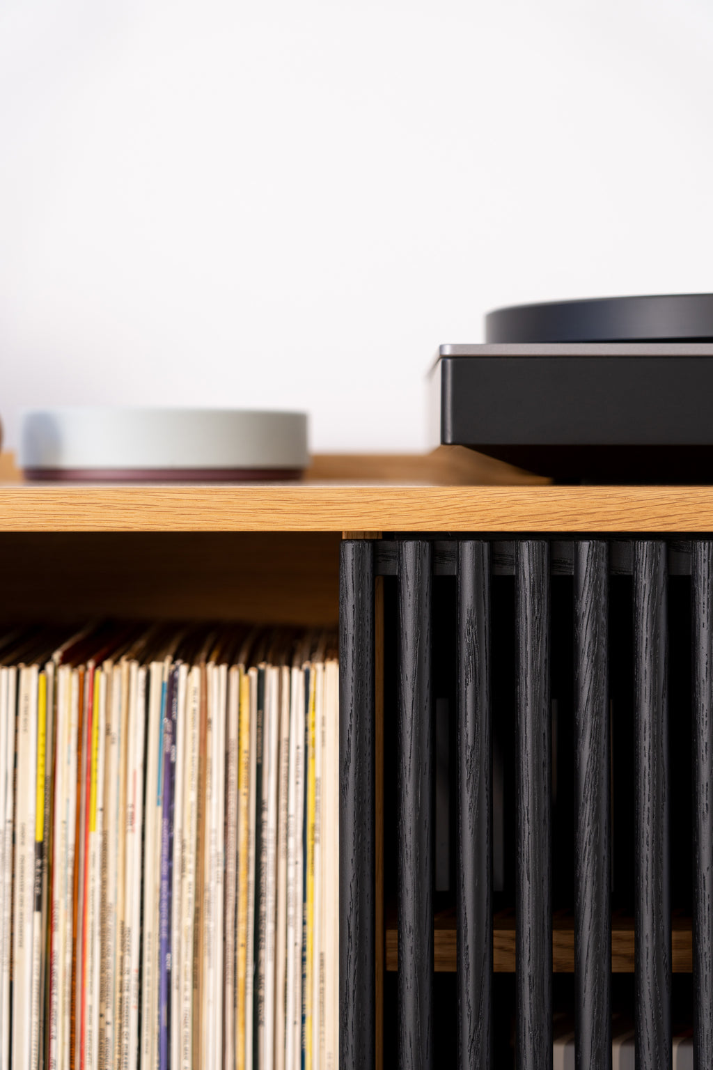 Close-up of a wood shelf with records and a modern turntable, featuring vertical black slats.