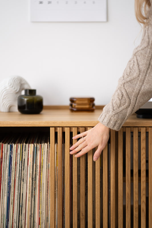 Hand reaching for vinyl records on a wooden shelf with decorative items on top.