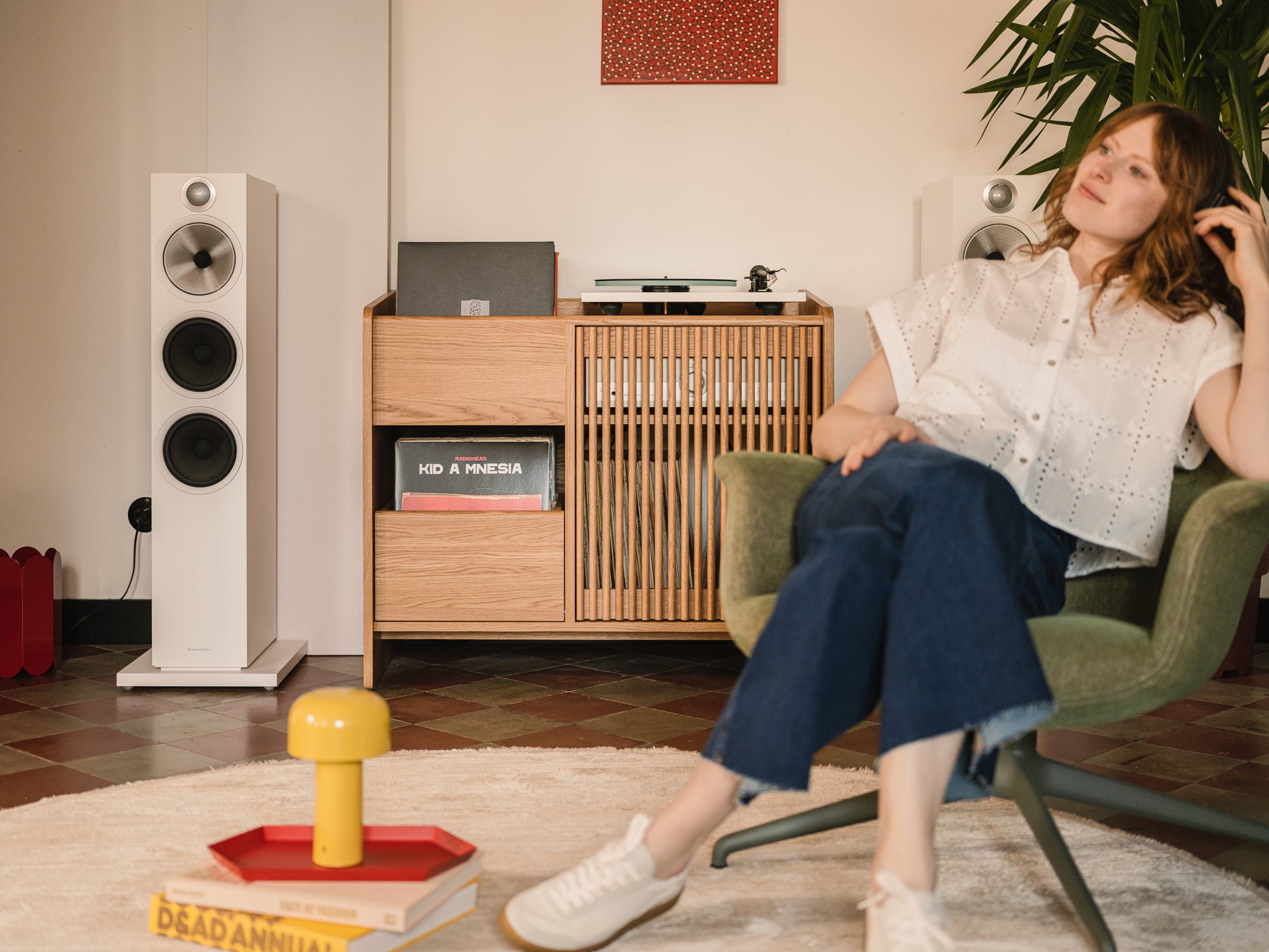 Woman relaxing in a chair with speakers and vinyl records on a wooden shelf in the background.