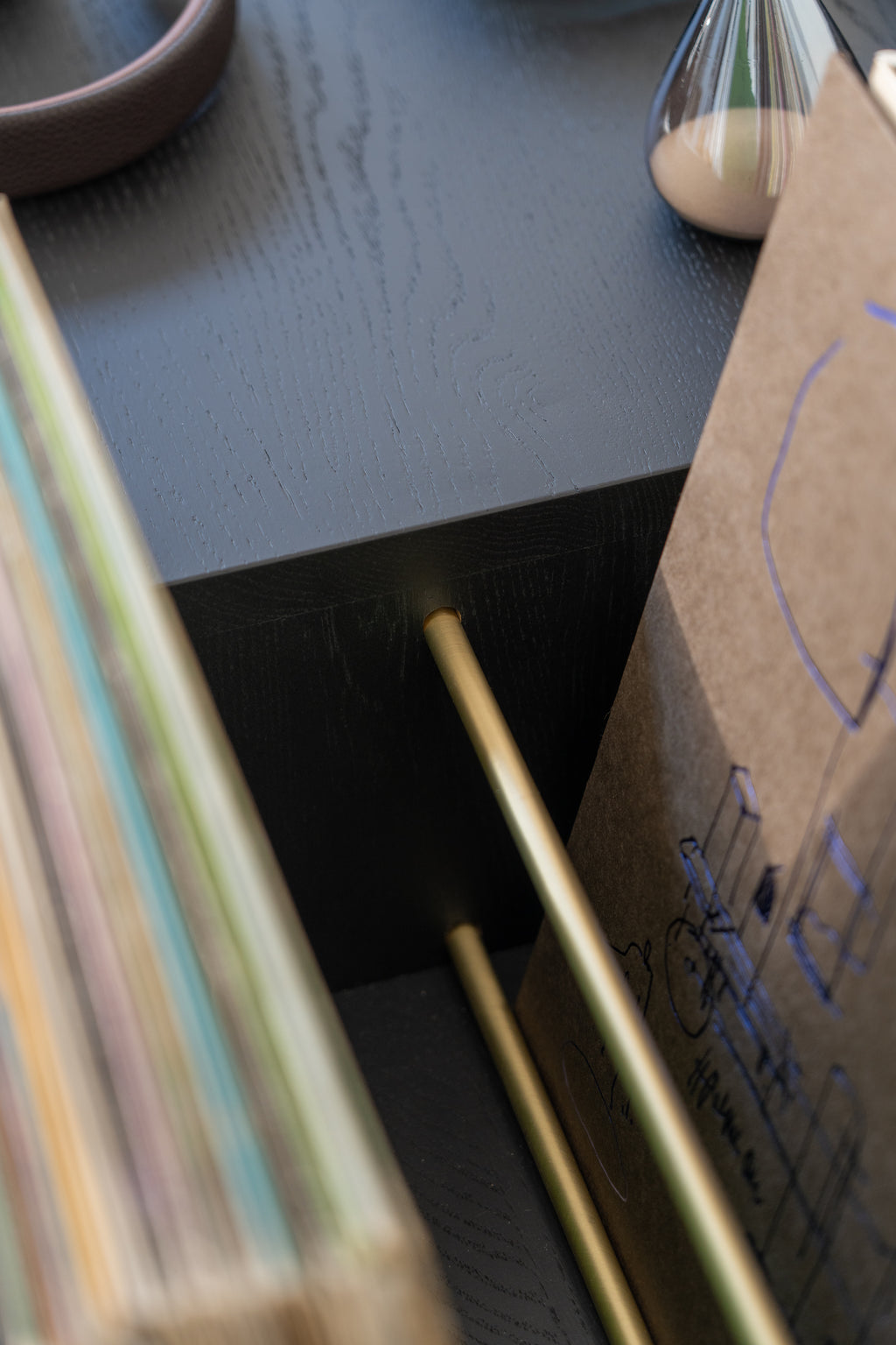 Close-up of a black shelf with papers, a decorative object, and gold rods.