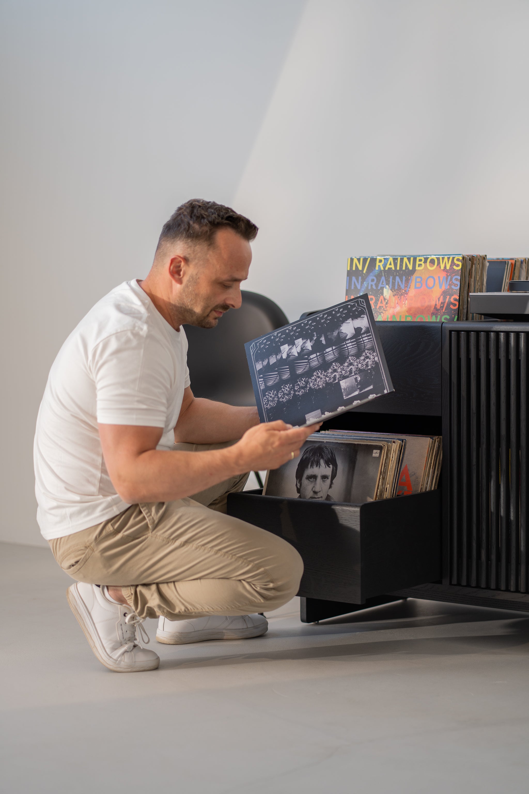 Man kneeling, browsing vinyl records on a shelf.