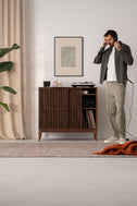 Man with headphones next to TONN 101 HIGH solid American walnut record player stand, right sliding front open
