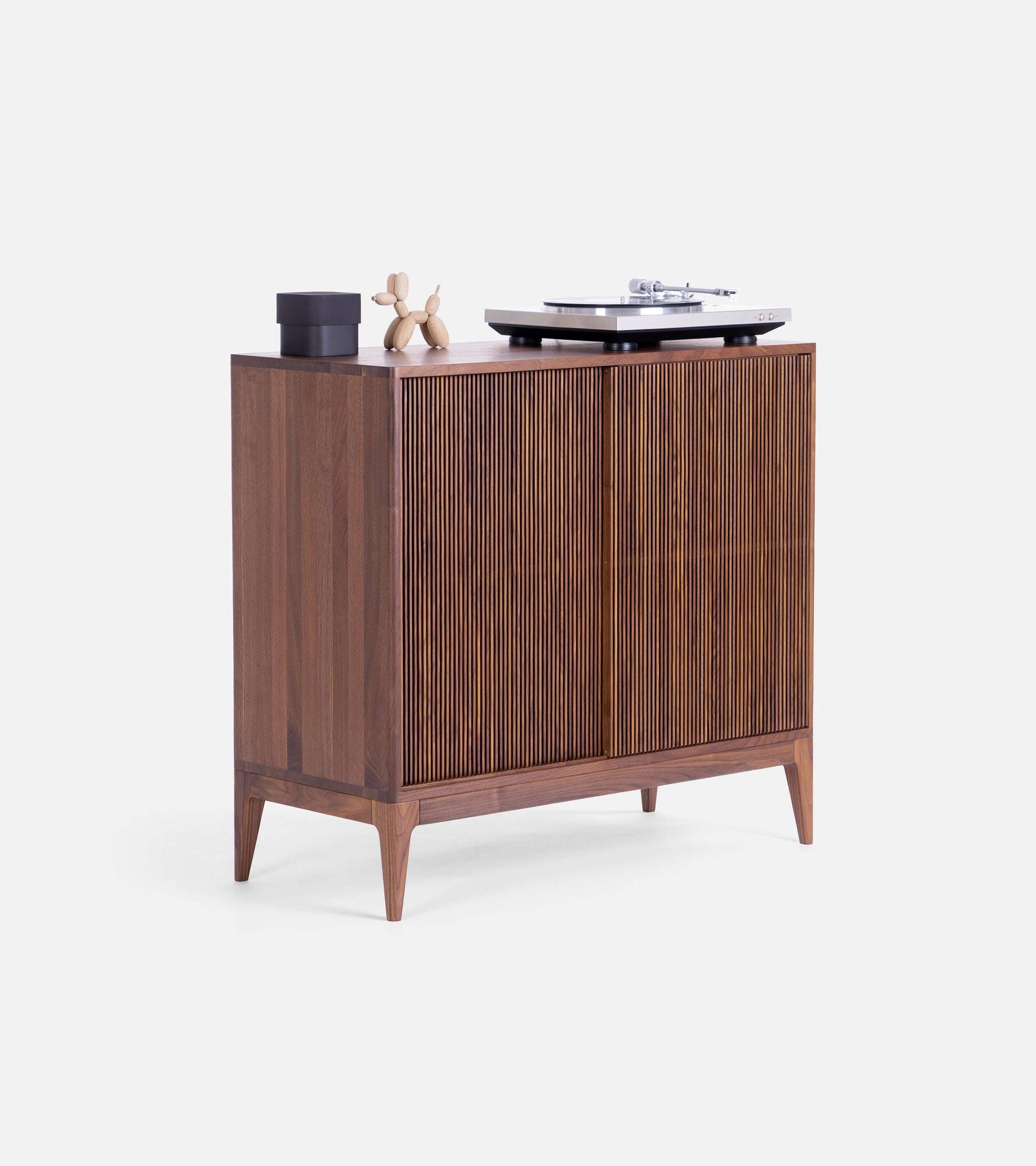 A wooden cabinet with decorative objects on top, including a small sculpture, a black container, and a record player.