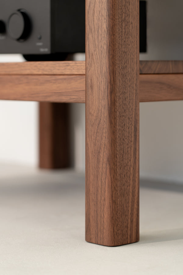 Close-up of a wooden furniture leg with a black electronic device on the shelf above.