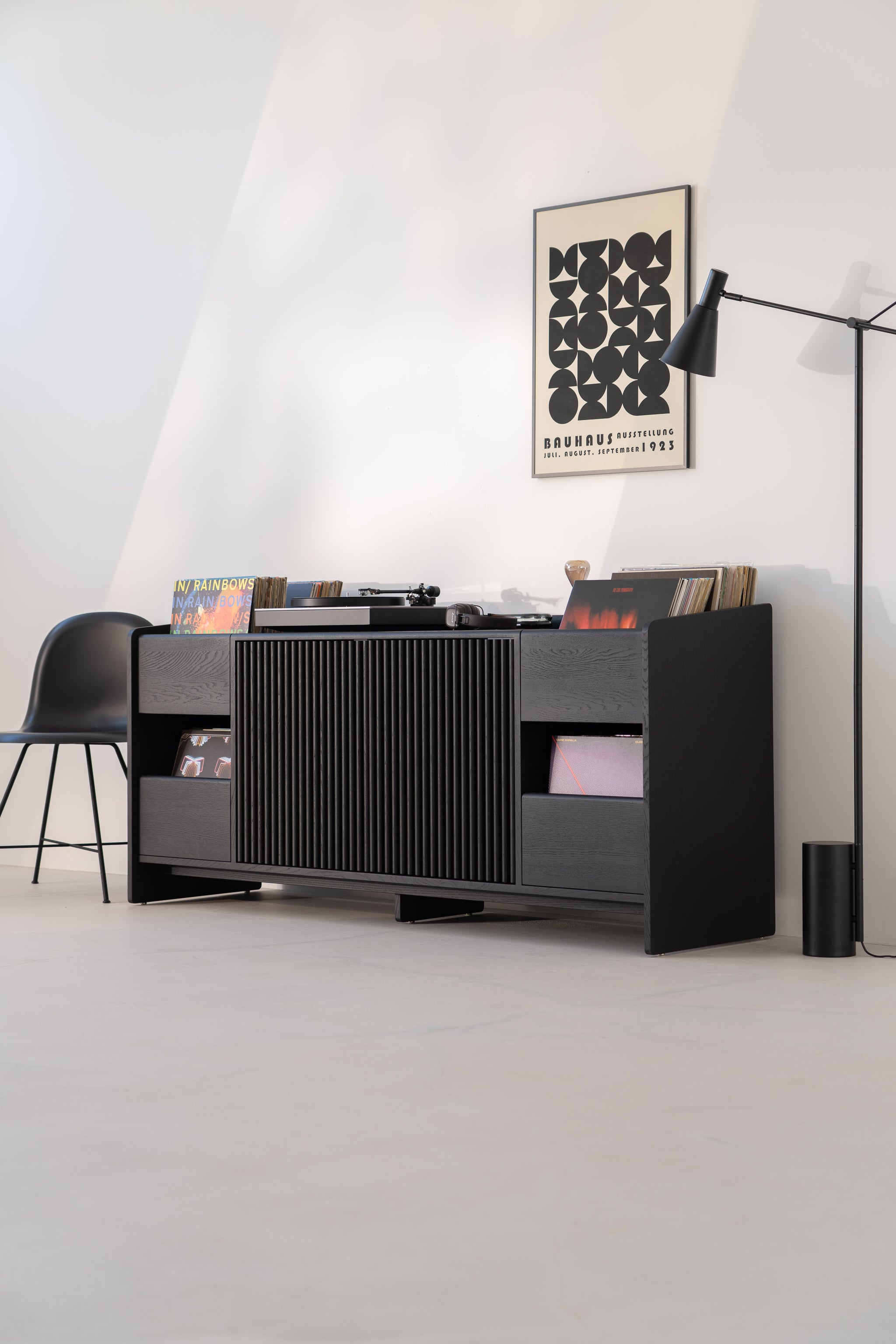 Modern living room with a black cabinet, turntable, records, chair, poster, and lamp.