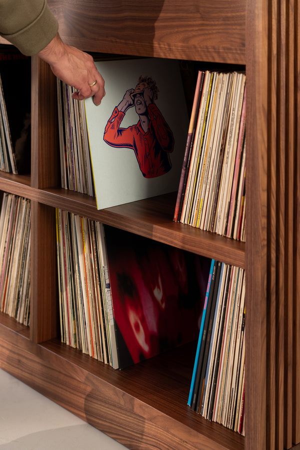 Hand selecting a vinyl record from a wooden shelf filled with albums.