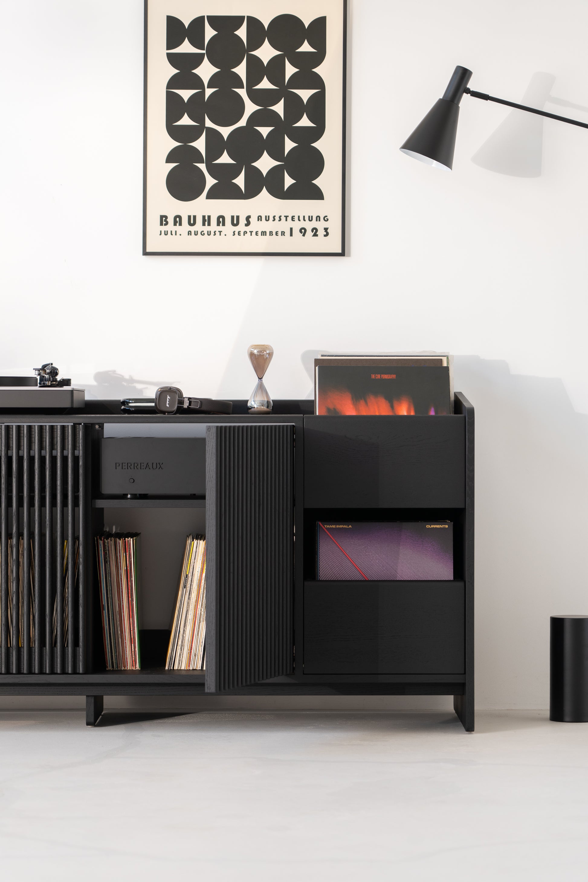 Black cabinet with records, poster, lamp, and turntable in a minimalist room.