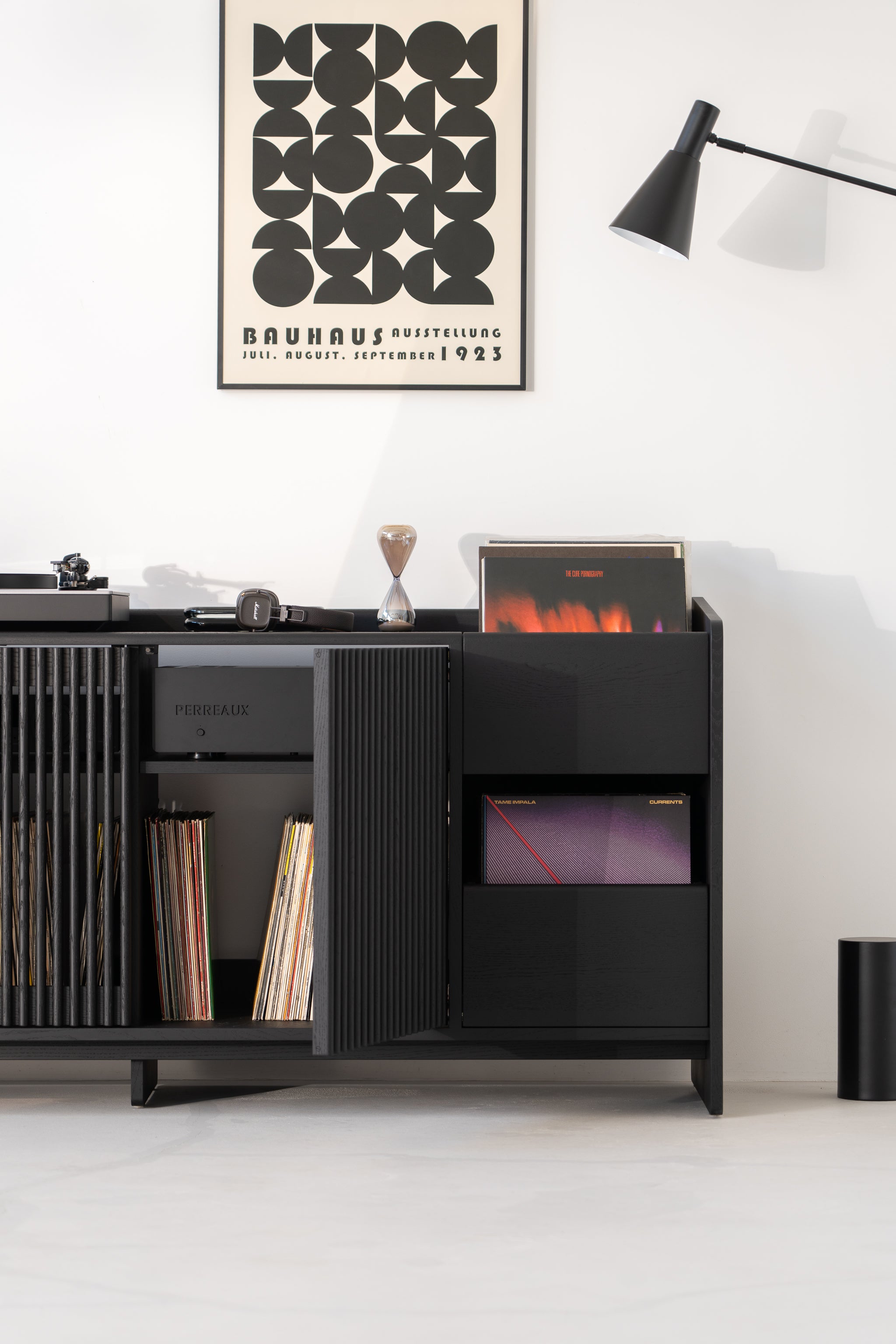 Black cabinet with records, poster, lamp, and turntable in a minimalist room.