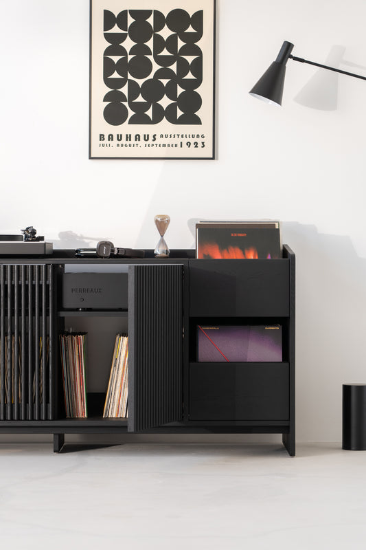 Black cabinet with records, poster, lamp, and turntable in a minimalist room.