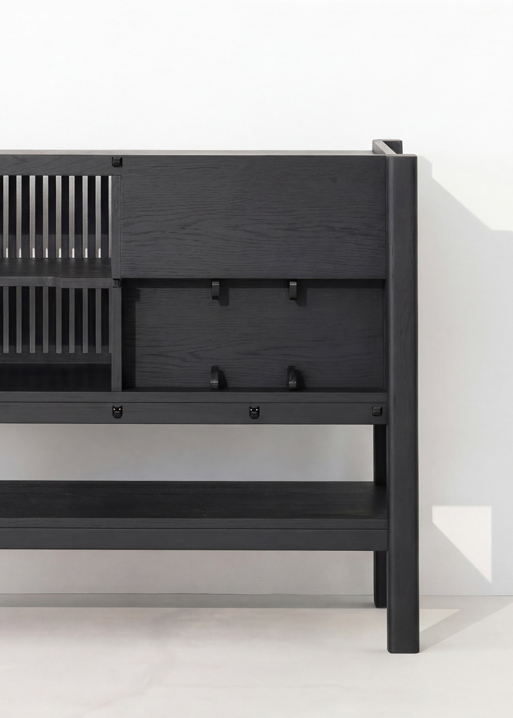 Black wooden sideboard with slatted shelves and closed cabinets against a white wall.