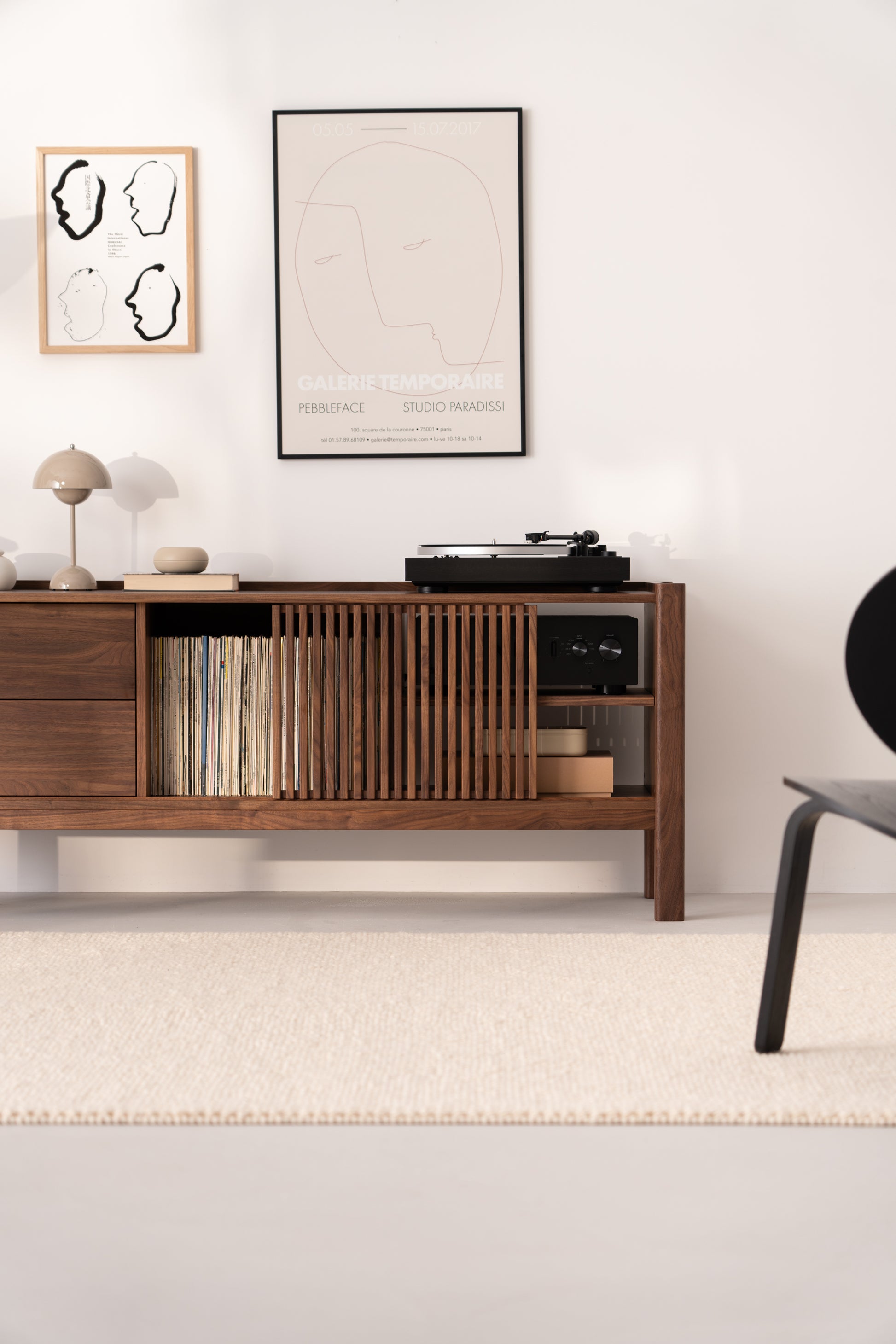 A minimalist room with a wooden console holding a record player, vinyl records, and books, under two framed artworks.