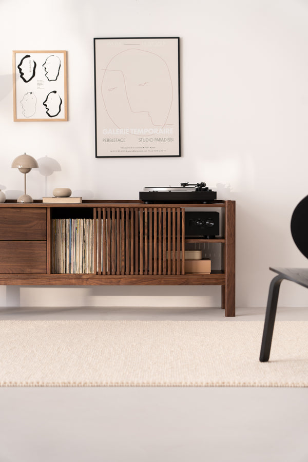 A minimalist room with a wooden console holding a record player, vinyl records, and books, under two framed artworks.