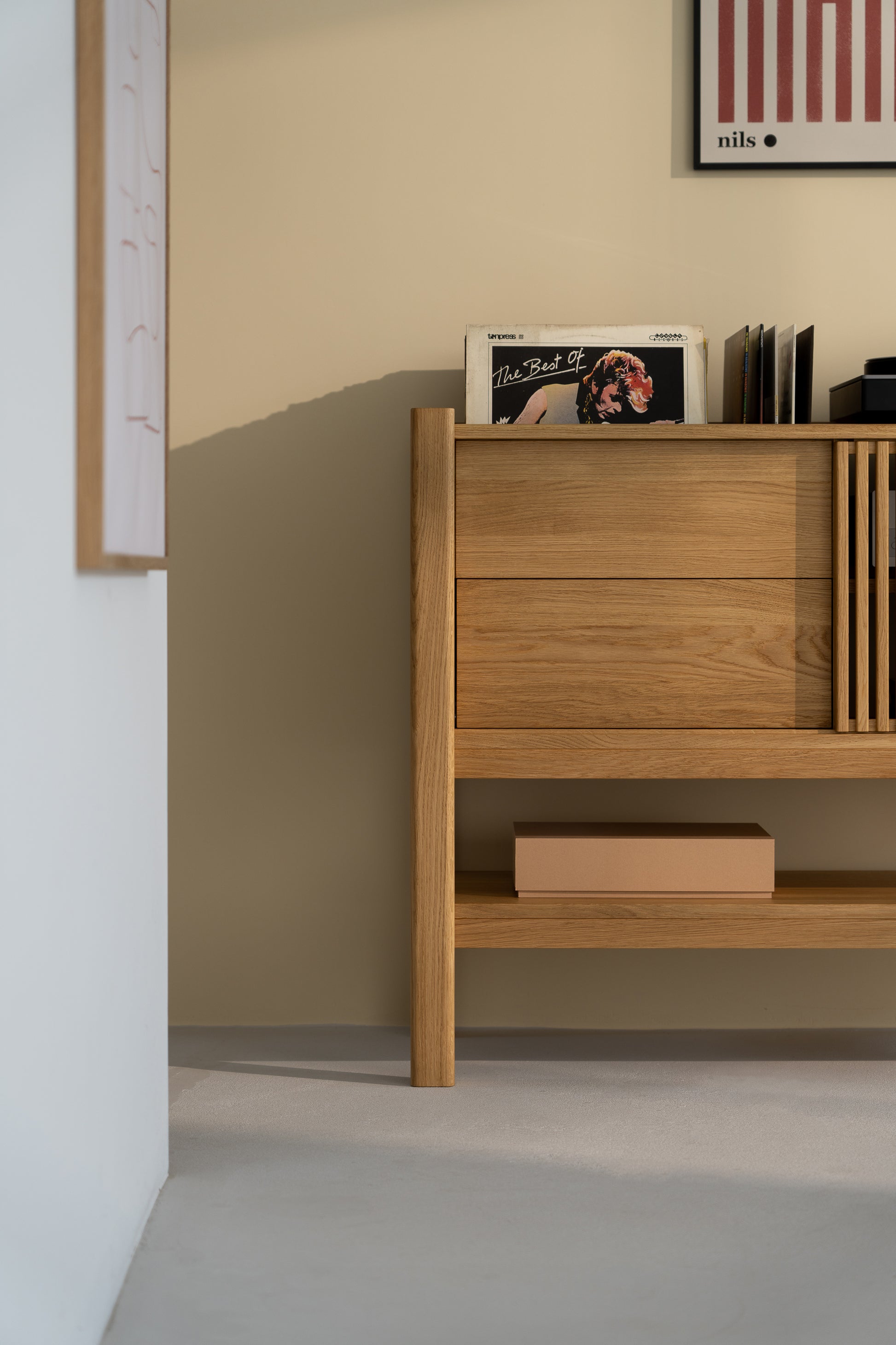 Wooden dresser with albums and a box, against a beige wall with framed art.