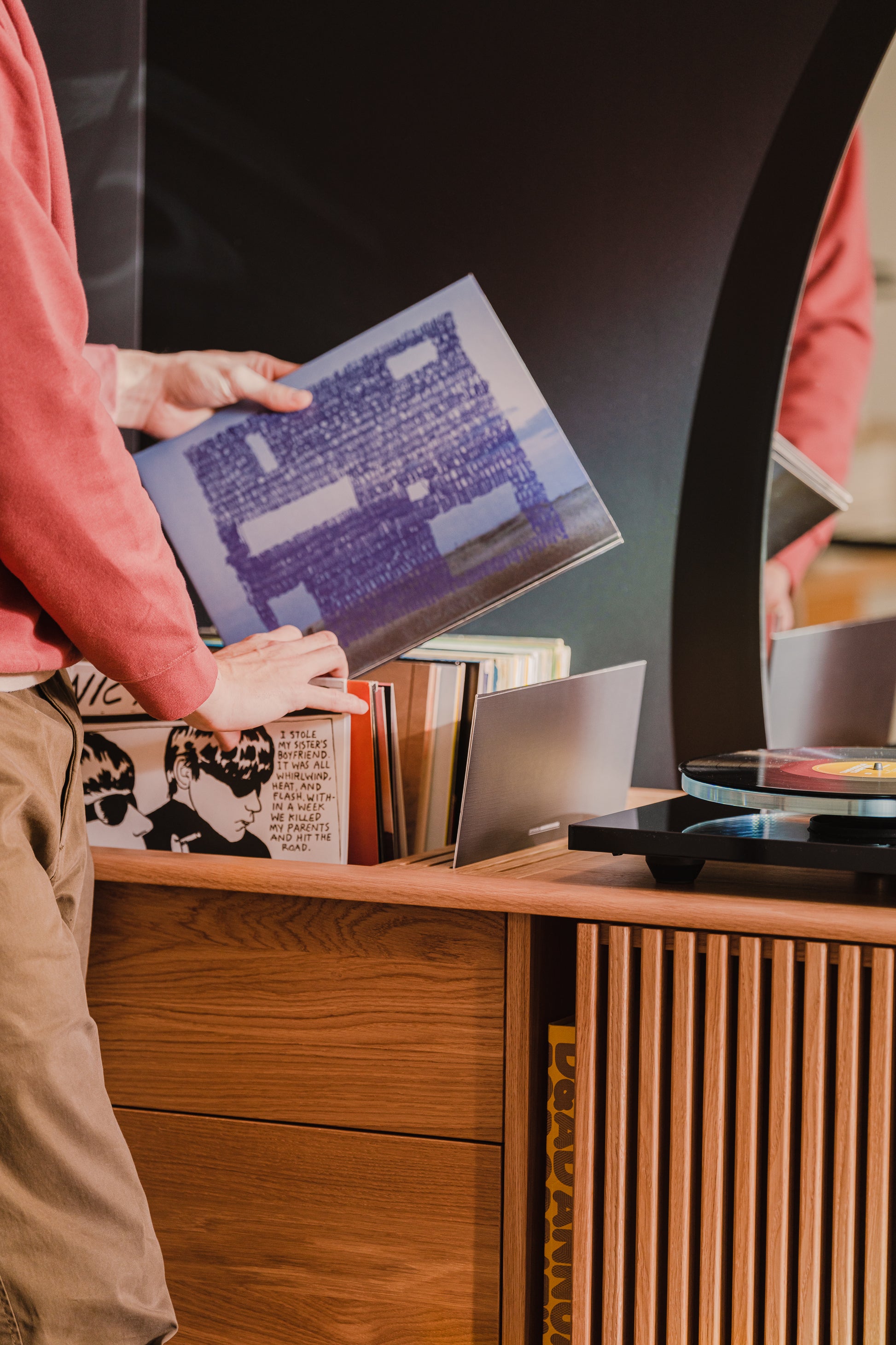 Person selecting records from a wooden cabinet beside a turntable.