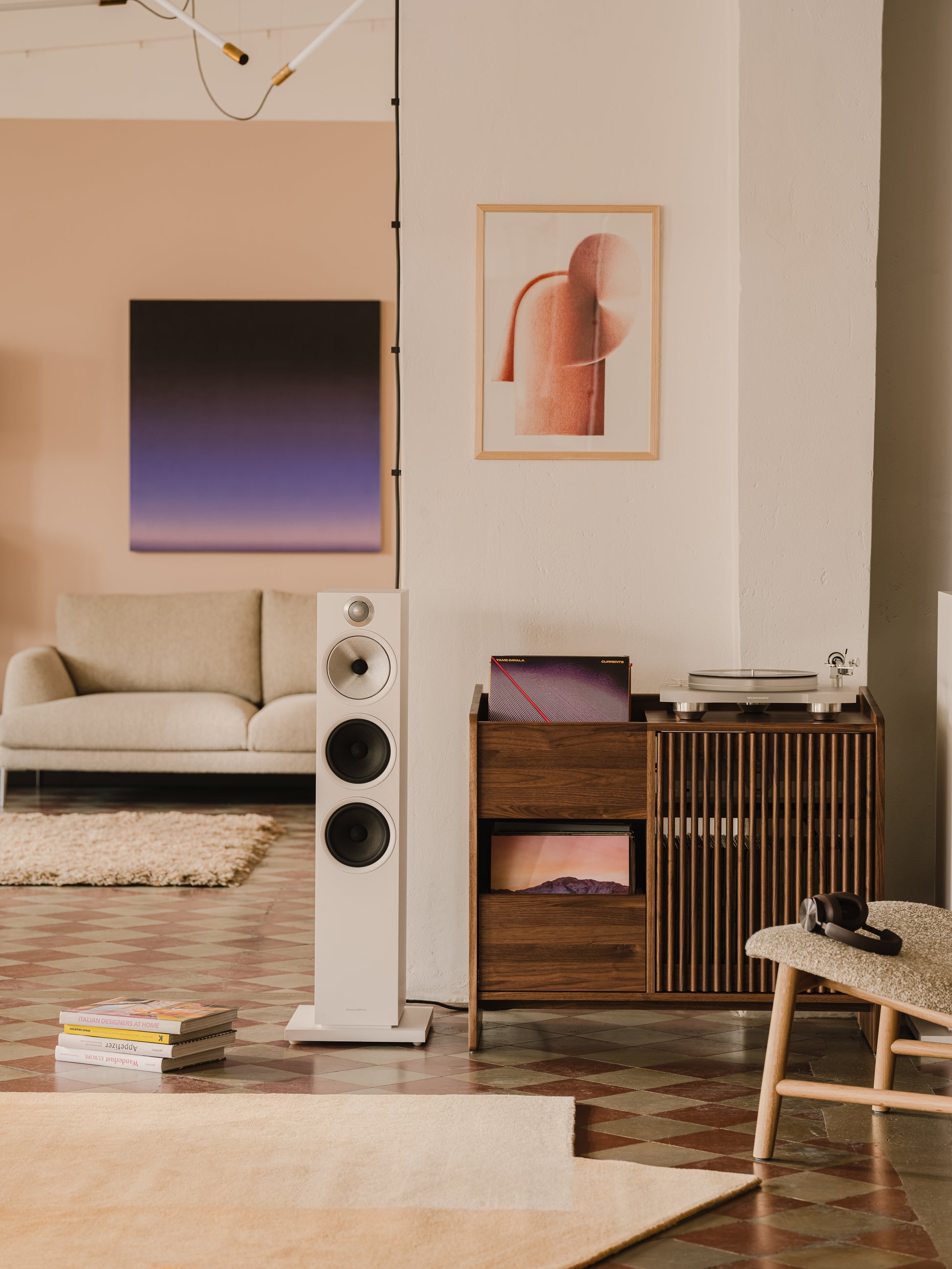 Modern living room with art, speakers, a turntable, and wooden storage. Neutral tones and geometric patterns.