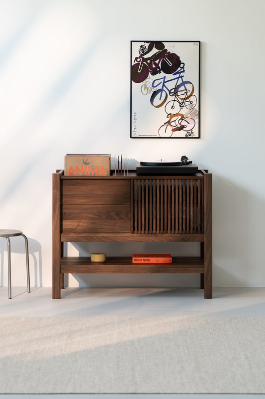 Wooden record console with vinyls and a turntable, abstract bicycle art on wall, and a small stool beside.