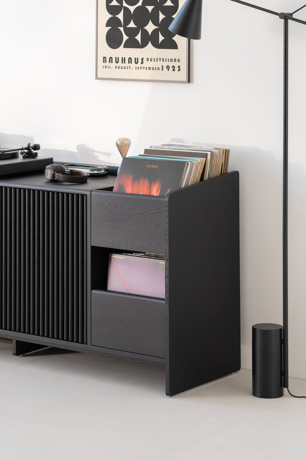 Black media console with vinyl records, turntable, headphones, and Bauhaus poster on the wall.