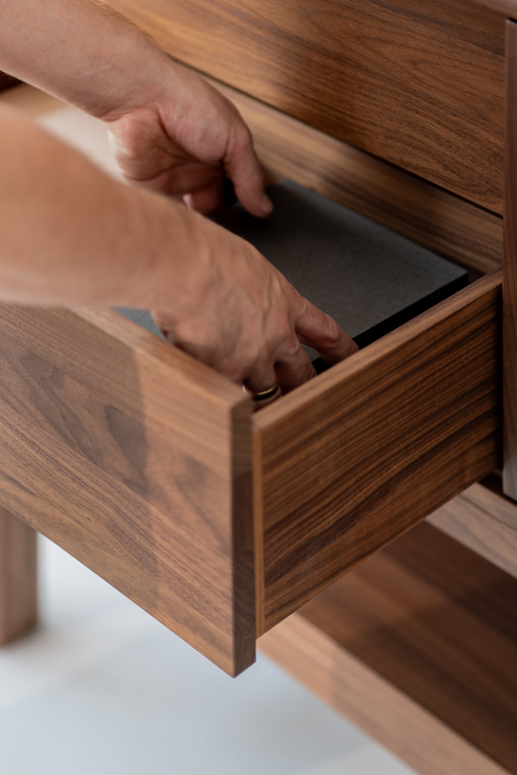 Hands opening a wooden drawer, placing a folder inside.
