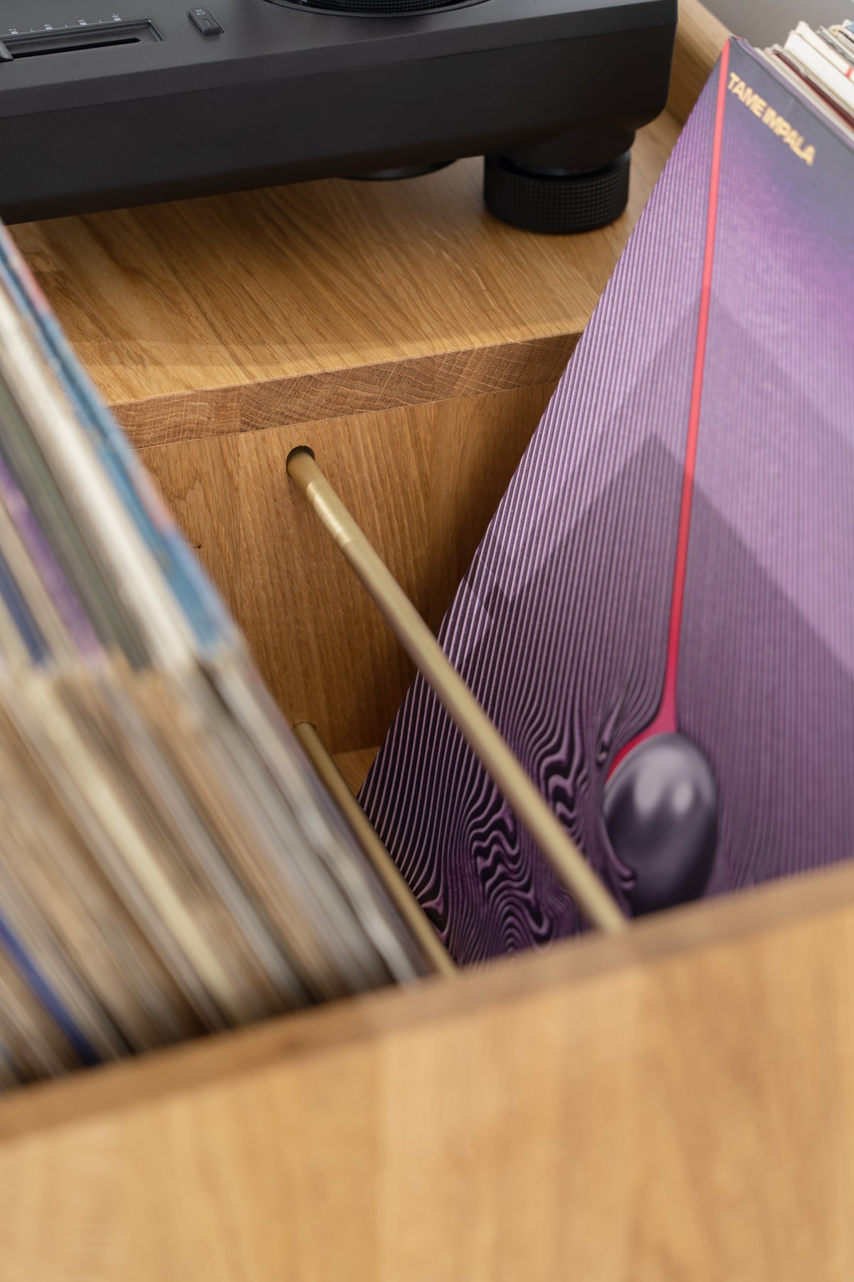 Close-up of the FUSE X in solid oak with a thin brass rod dividing records in the top niche beneath the turntable