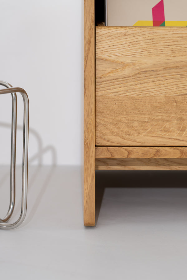 Side close-up of the FUSE X in solid oak showing the bottom drawer front, base rail and side panel reaching the floor