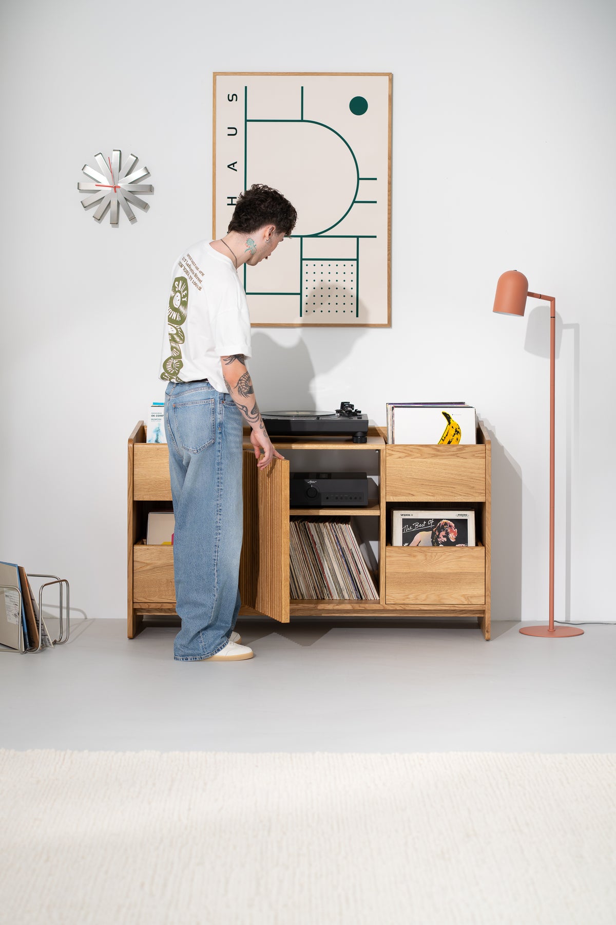A man opens the slatted door of the FUSE X in solid oak, revealing an amplifier on a shelf and records below
