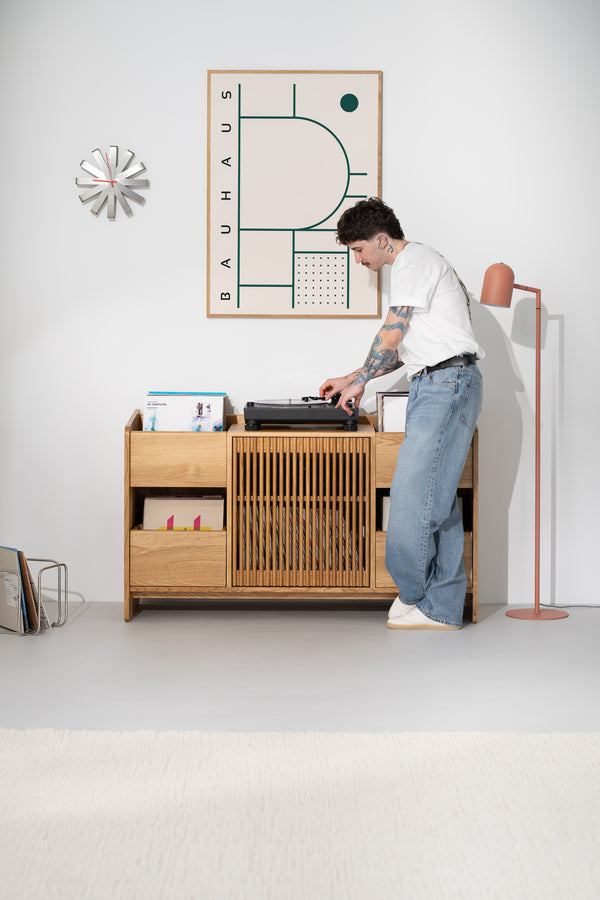 FUSE X record player storage in solid oak, front view with a man playing a record on the turntable