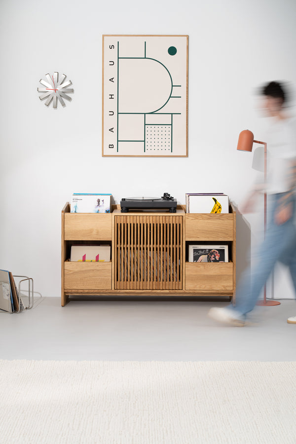 FUSE X in solid oak seen from the front as a blurred person walks past, with a turntable and records on top
