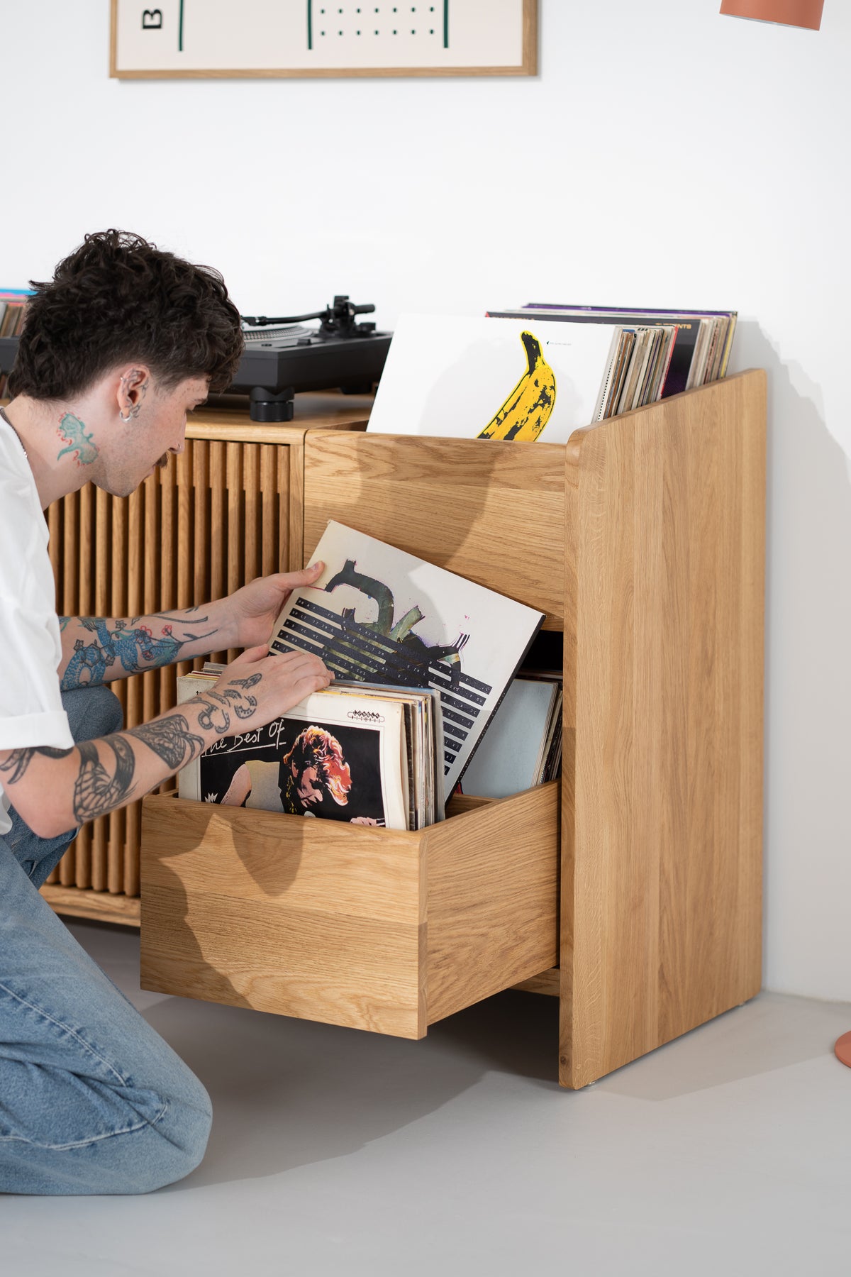 A man kneels beside the FUSE X in solid oak, browsing records in an open side drawer with a central divider