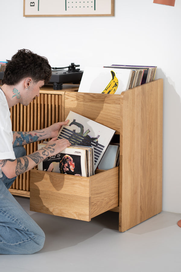 A man kneels beside the FUSE X in solid oak, browsing records in an open side drawer with a central divider