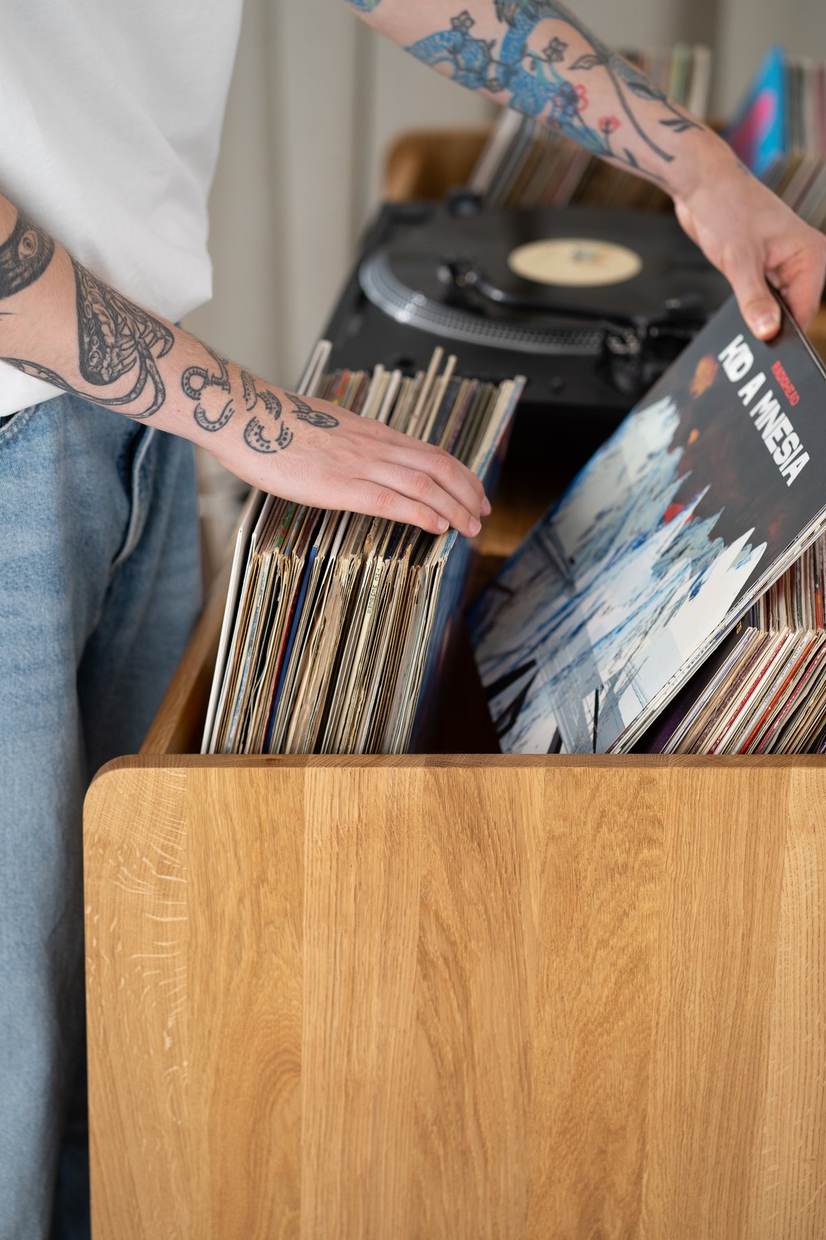 Hands flipping through records in the top niche of the FUSE X in solid oak, beside the turntable