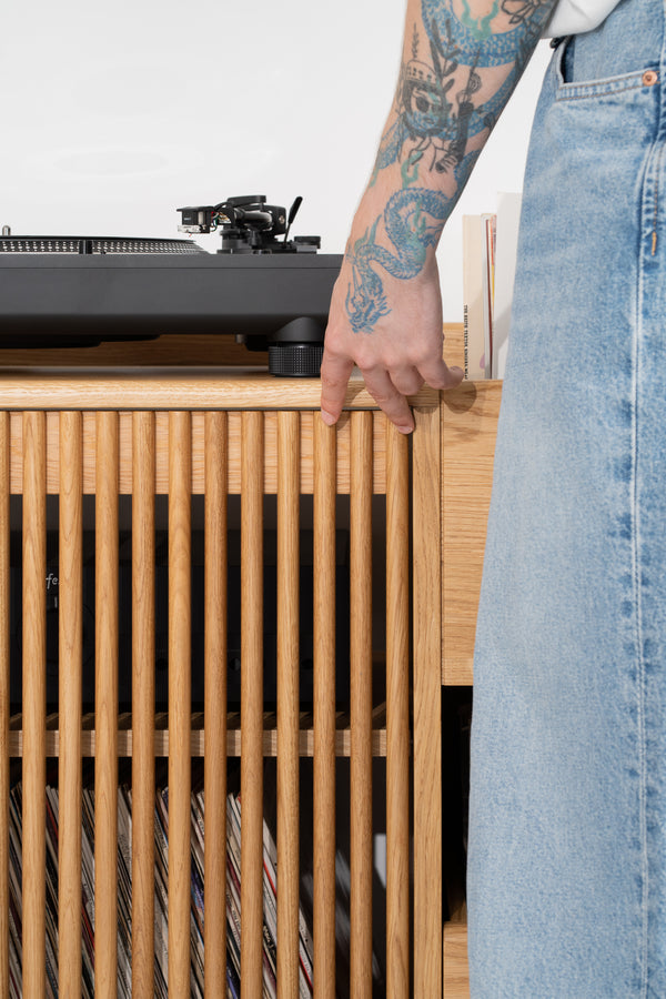 FUSE X in solid oak, close-up of door slats with records behind them and a hand on the top edge beside a turntable