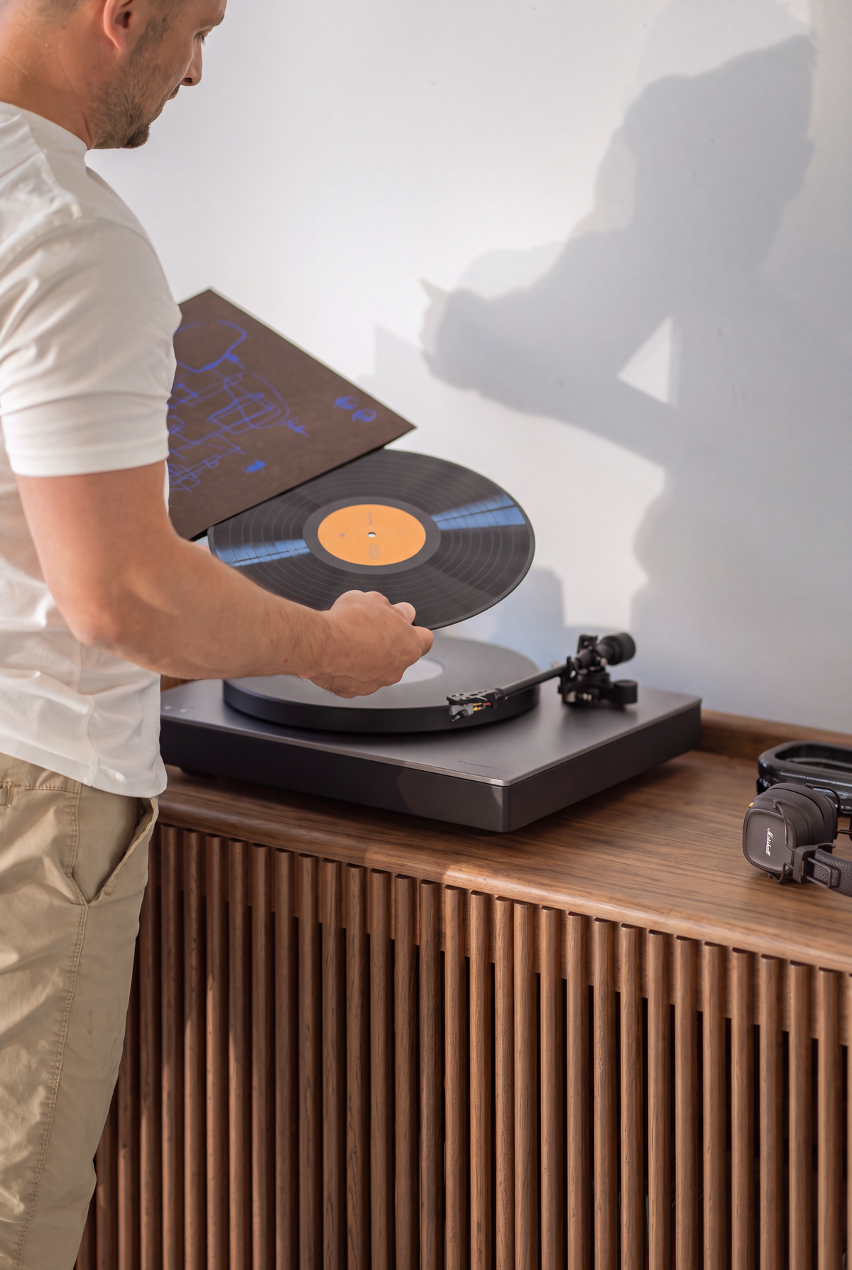 A man places a record on the turntable atop the FUSE XX in solid walnut, above the slatted doors