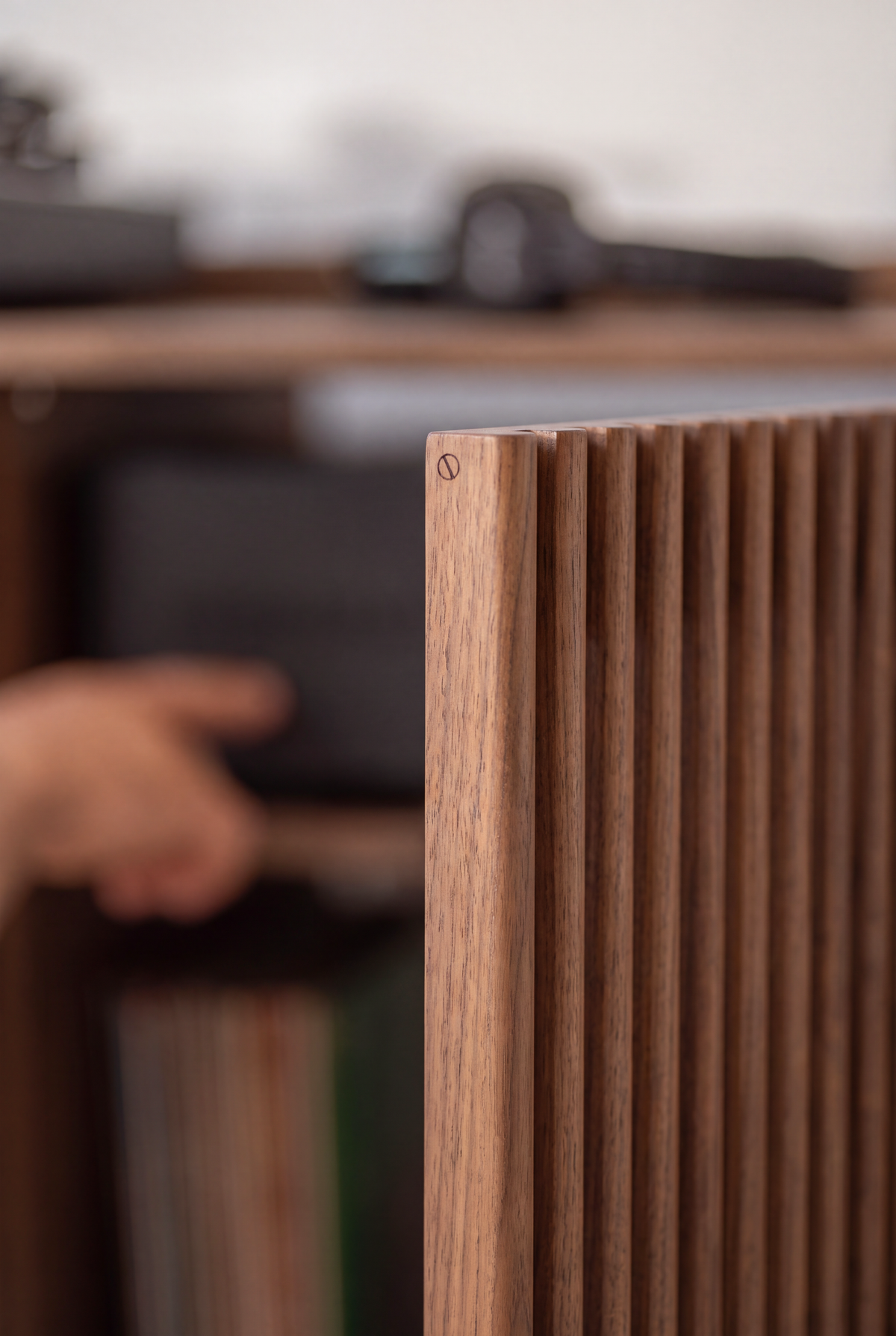FUSE XX in solid walnut, close-up of the edge of an open slatted door with a blurred hand reaching behind it