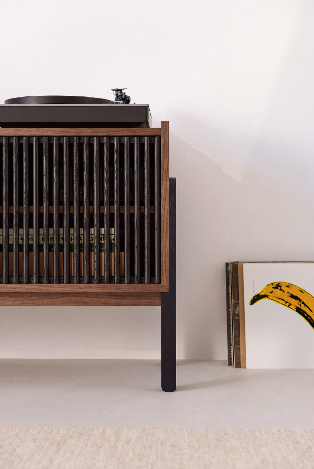 One end of VIBE in solid walnut, with records visible through the closed black slatted front and a turntable above