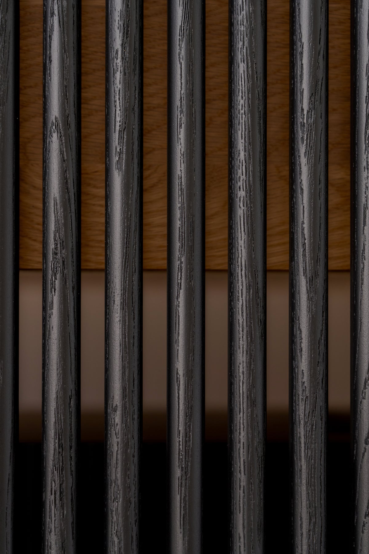 Macro of rounded black slats with visible open grain on VIBE in solid walnut, with the walnut interior behind