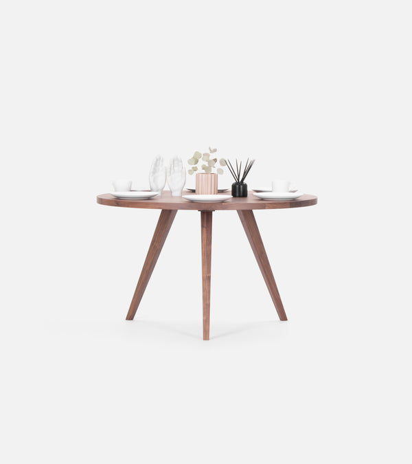 Round wooden table set for two, featuring cups, saucers, decorative white hands, a small plant, and a black reed diffuser.