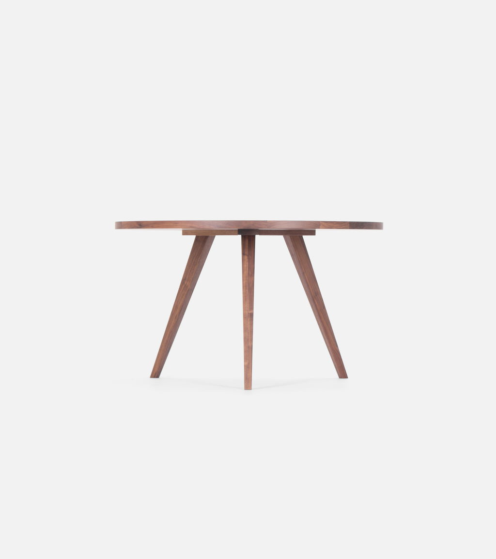 OKKO round table in solid American walnut with three angled legs, bare, against a white background