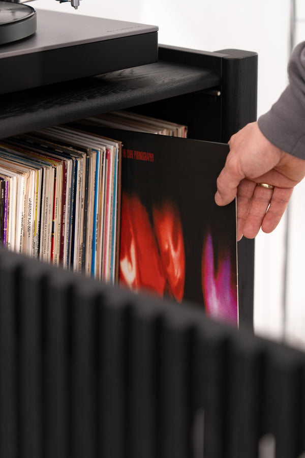 Hand selecting a vinyl record from a shelf beside a turntable.