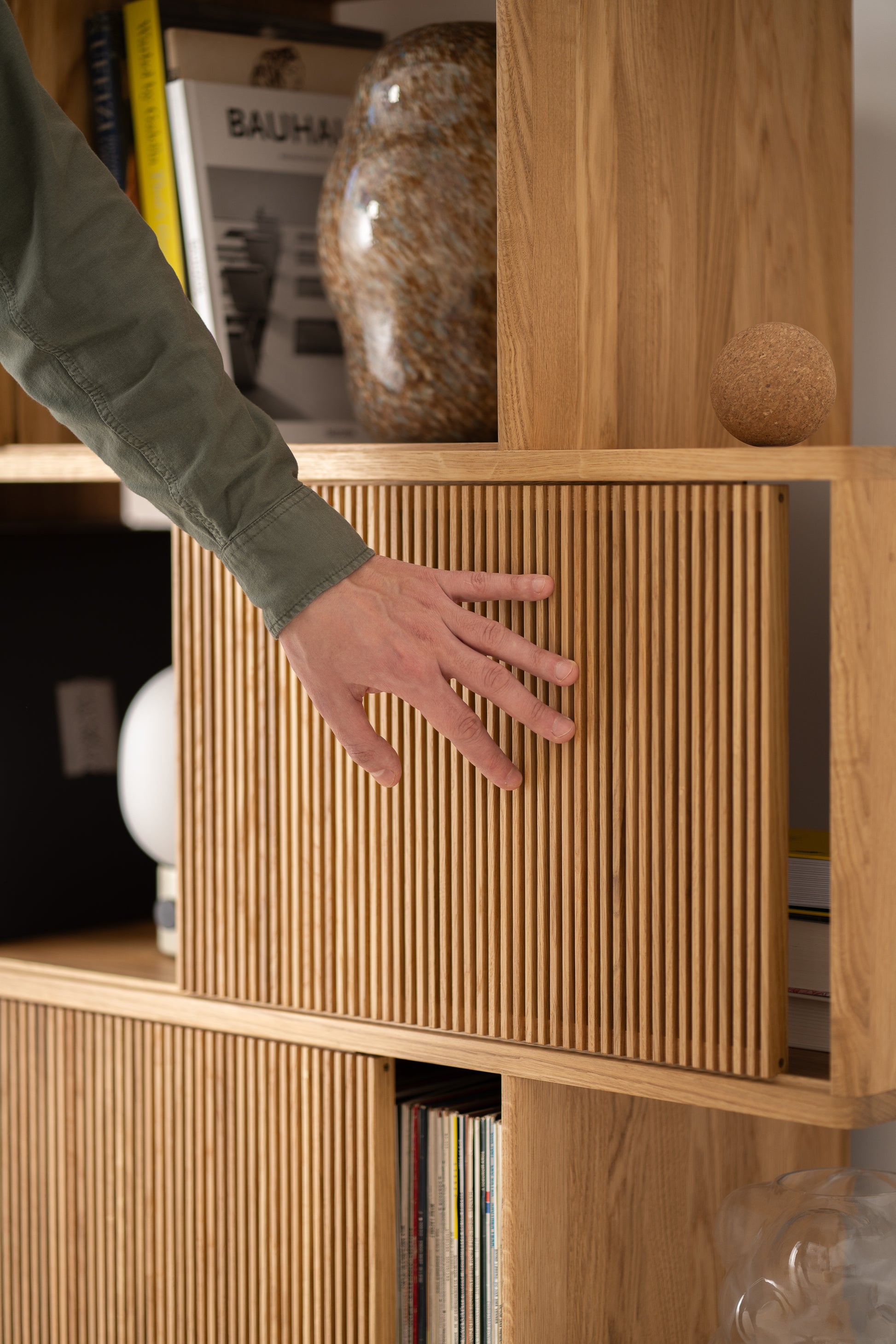Hand touching a wooden cabinet with vertical slats, books and decor seen in the background.