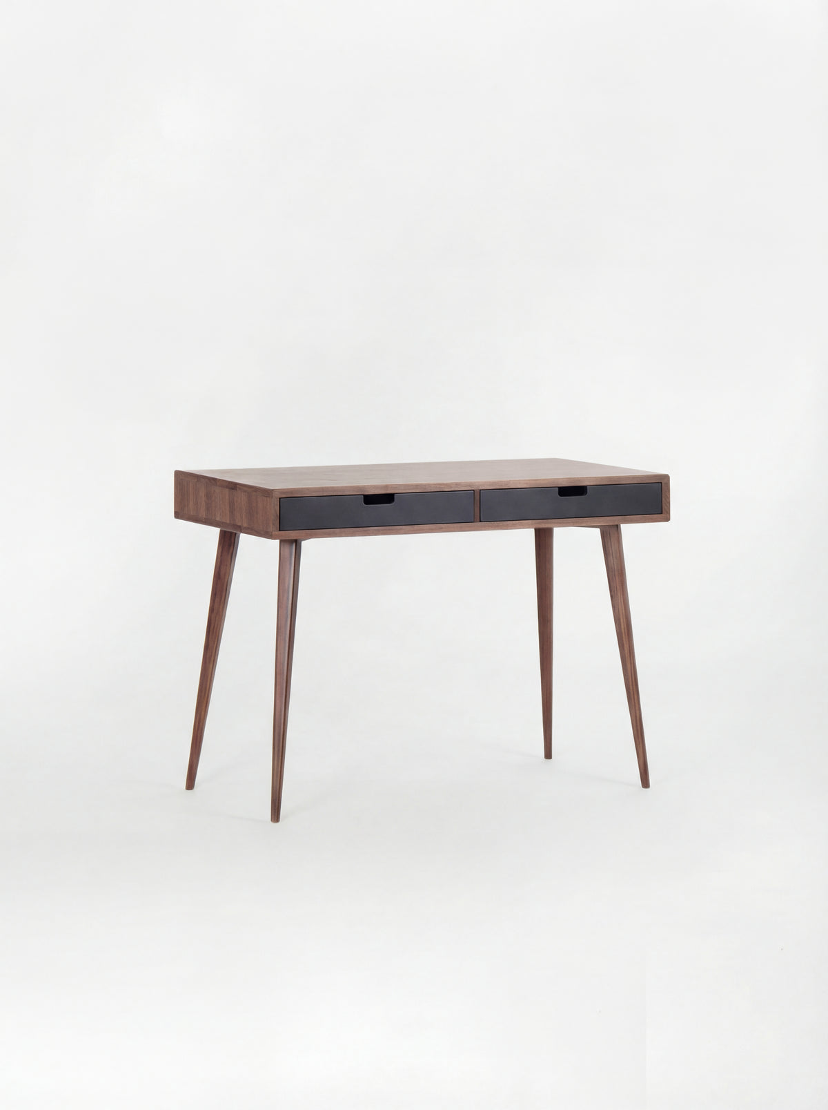Empty HEIM 105 desk in solid walnut with two black drawer fronts, angled against a plain white background