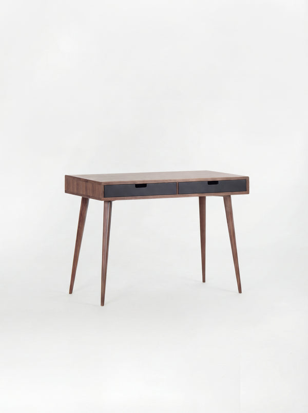 Empty HEIM 105 desk in solid walnut with two black drawer fronts, angled against a plain white background