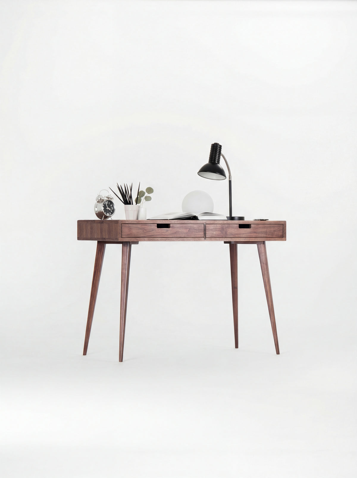 HEIM 105 small desk in solid walnut with a black desk lamp, globe lamp and open book, seen at a slight angle