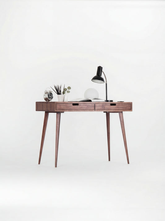 HEIM 105 small desk in solid walnut with a black desk lamp, globe lamp and open book, seen at a slight angle