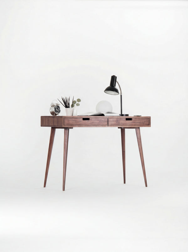 HEIM 105 small desk in solid walnut with a black desk lamp, globe lamp and open book, seen at a slight angle