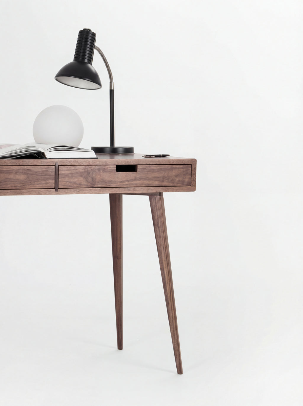 Right half of the HEIM 105 desk in solid walnut, with a black desk lamp, globe lamp, open book and two splayed legs