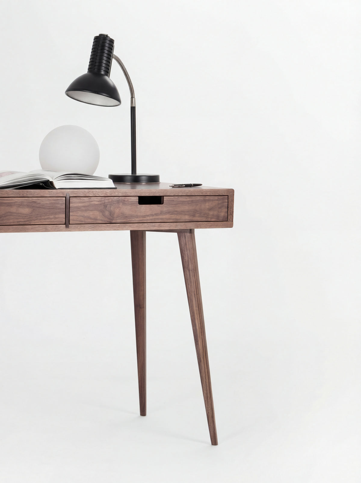 Right half of the HEIM 105 desk in solid walnut, with a black desk lamp, globe lamp, open book and two splayed legs